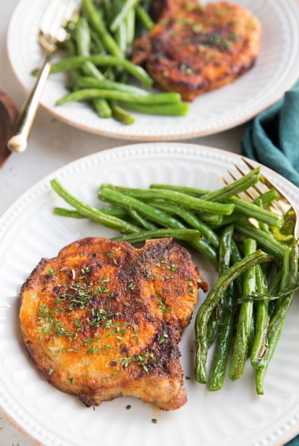 Air Fryer Pork Chops and air fryer green beans together on a white plate with a gold fork, ready to serve. Blue napkin to the side.