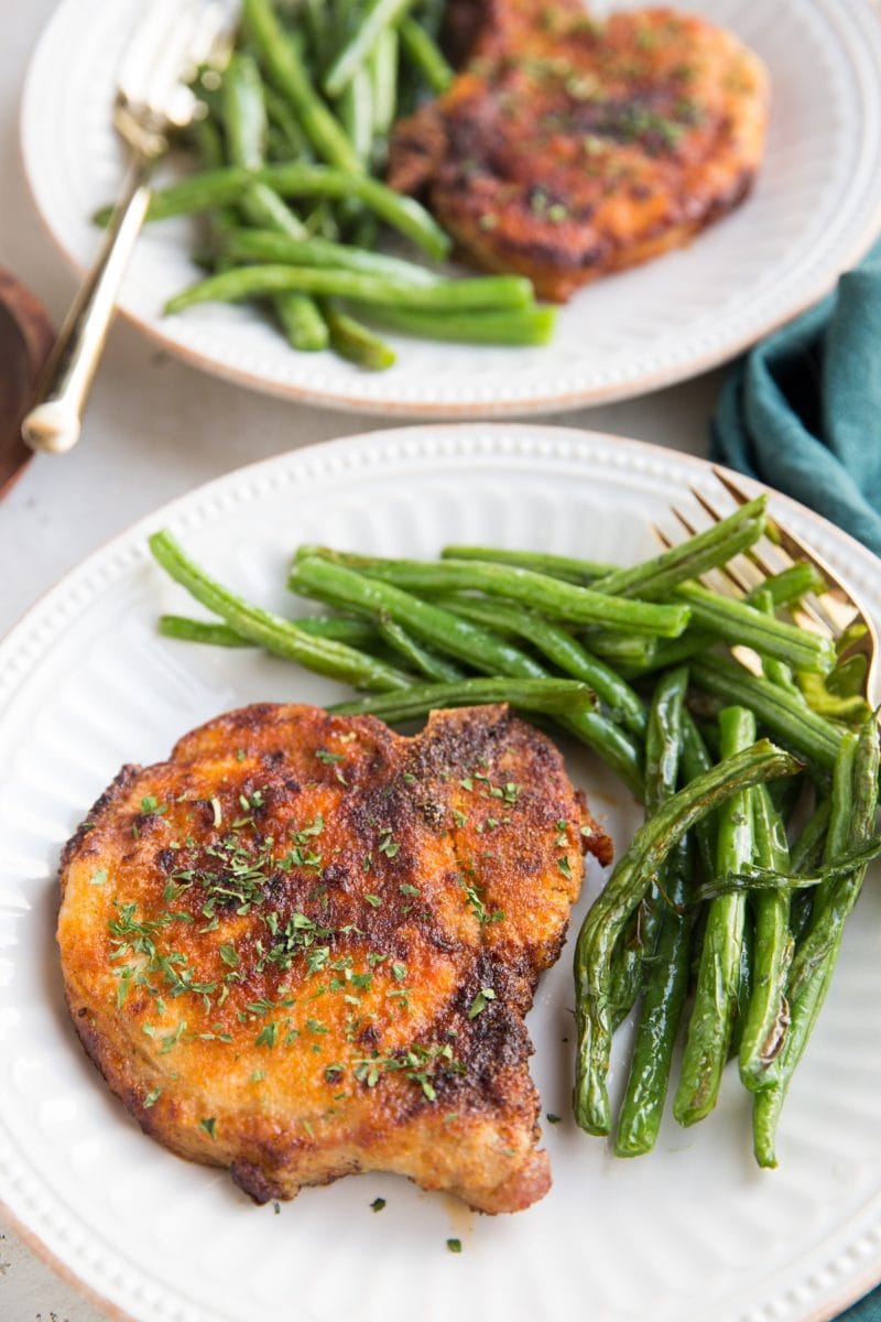 Air Fryer Pork Chops and air fryer green beans together on a white plate with a gold fork, ready to serve. Blue napkin to the side.