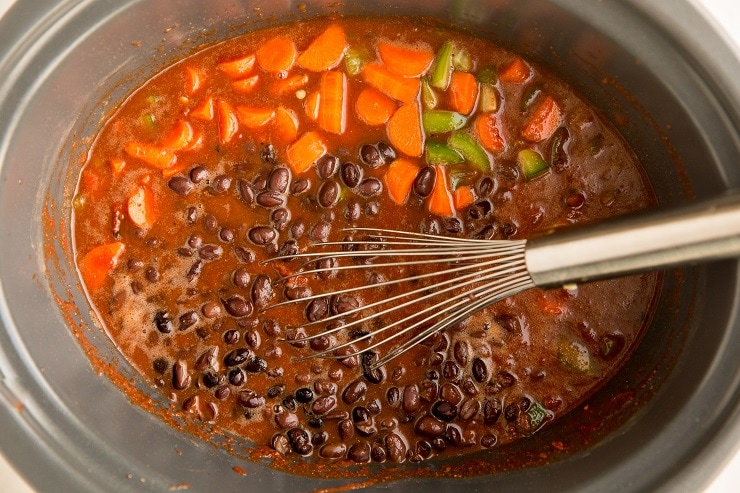 Stir crushed tomatoes, broth, chili powder, cocoa powder, black beans, carrots and peppers together in the clay pot