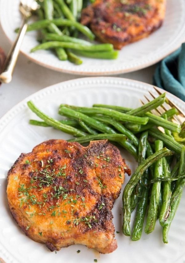 Air Fryer Pork Chops and air fryer green beans together on a white plate with a gold fork, ready to serve. Blue napkin to the side.