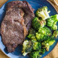 Blue plate with steak and broccoli on it with a gold fork to the side and a golden napkin