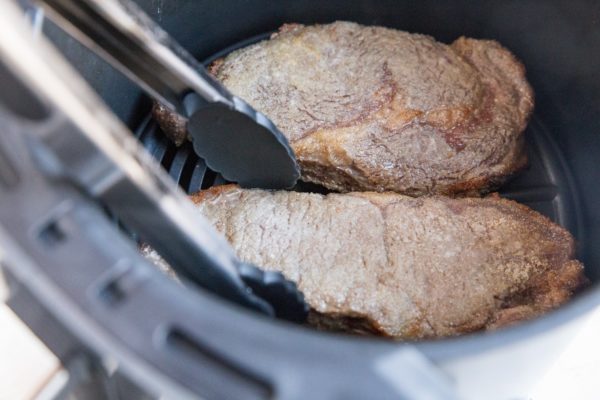 Tongs flipping steaks half way through the air fry process