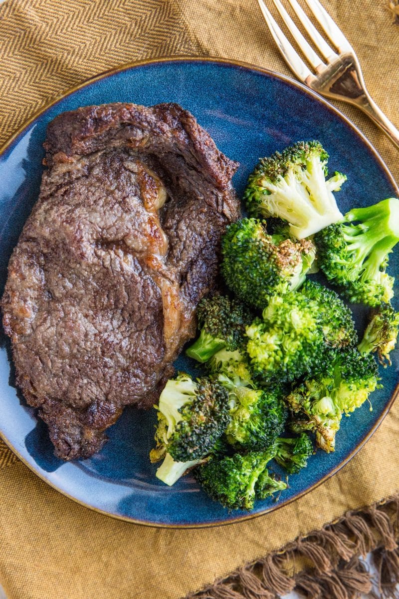 Blue plate with steak and broccoli on it with a gold fork to the side and a golden napkin