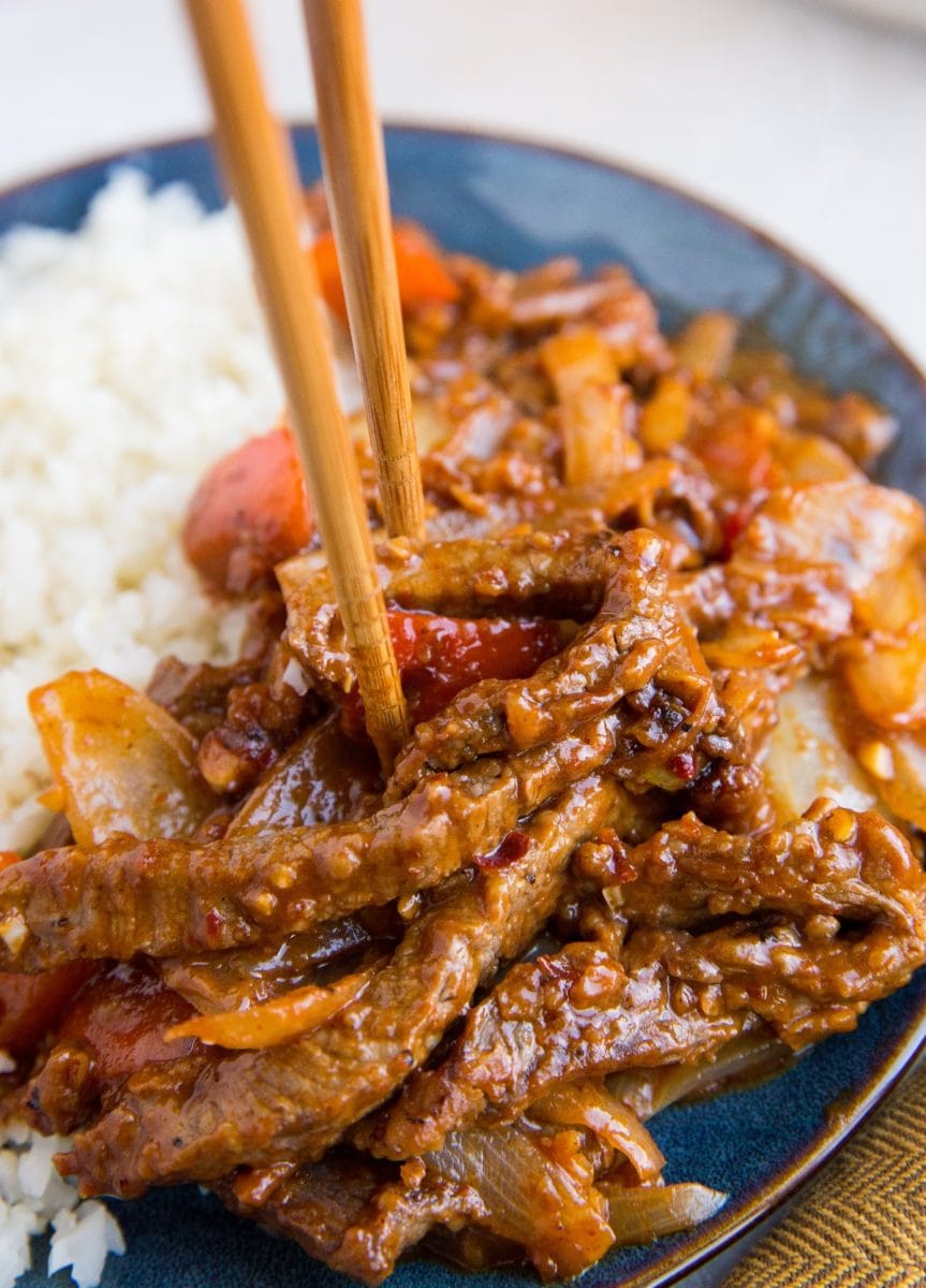 Close up of chopsticks taking a portion of Beijing Beef off a blue plate