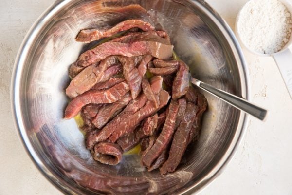 Strips of raw beef in a mixing bowl with whisked egg