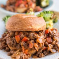 Close up image of a sloppy joe on a plate with a plate of sloppy joes in the background.