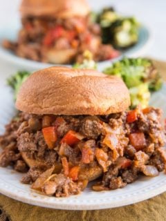 Close up image of a sloppy joe on a plate with a plate of sloppy joes in the background.