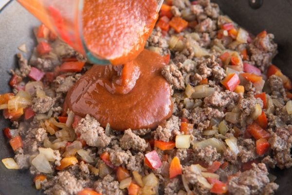 Sloppy joe sauce being poured into the skillet with meat