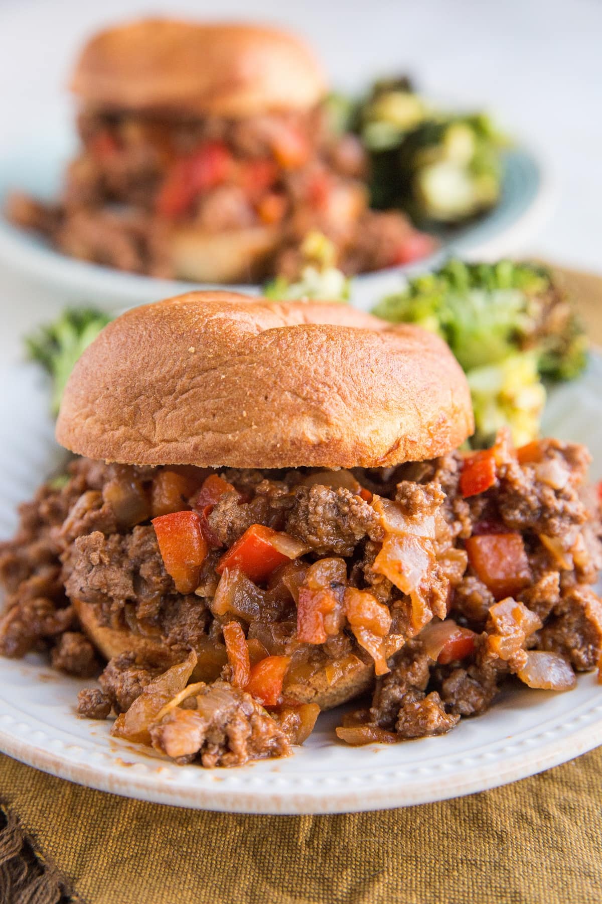 Close up image of a sloppy joe on a plate with a plate of sloppy joes in the background.