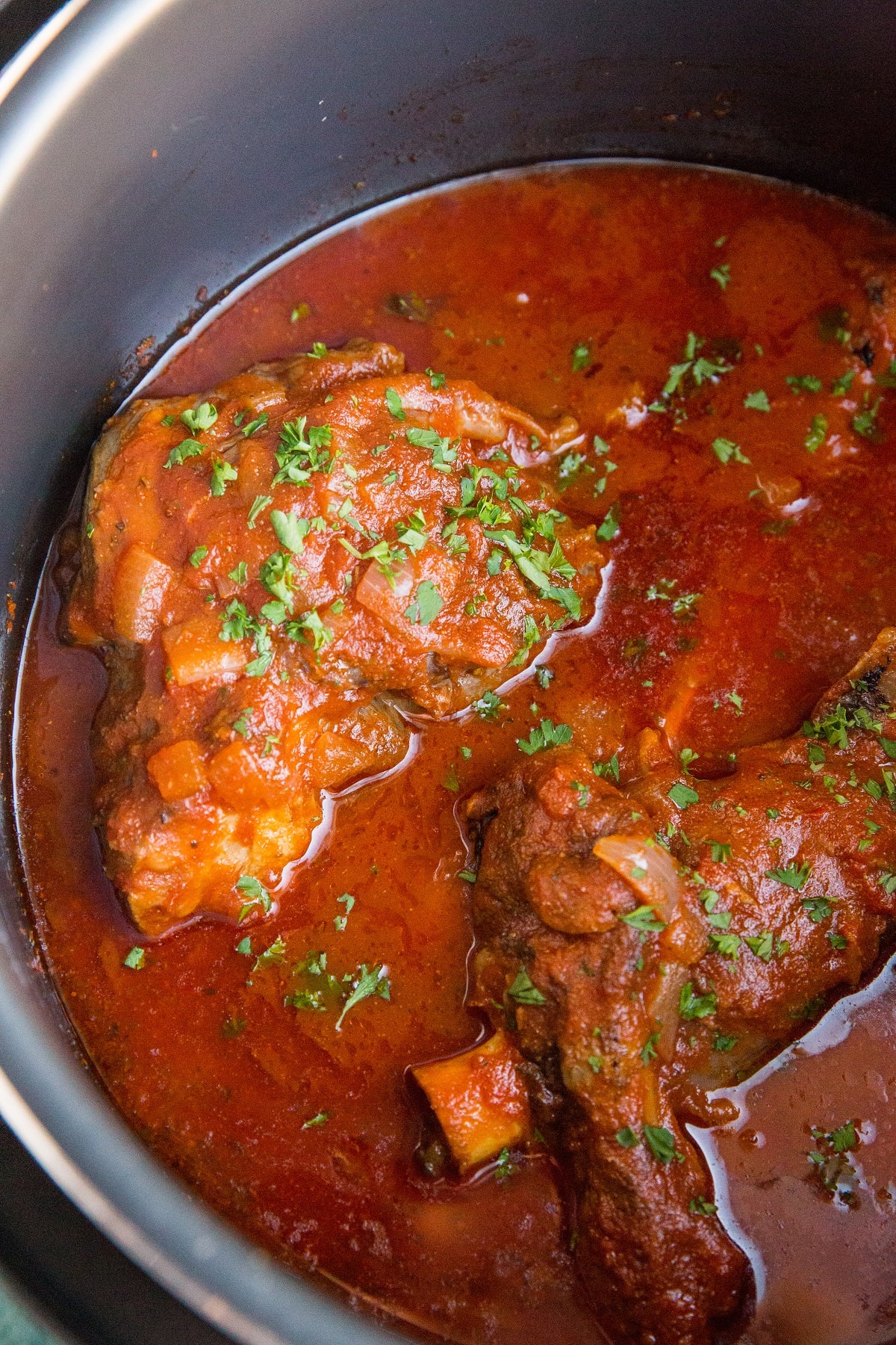 Crock pot full of lamb shanks cooked in a red wine tomato sauce.
