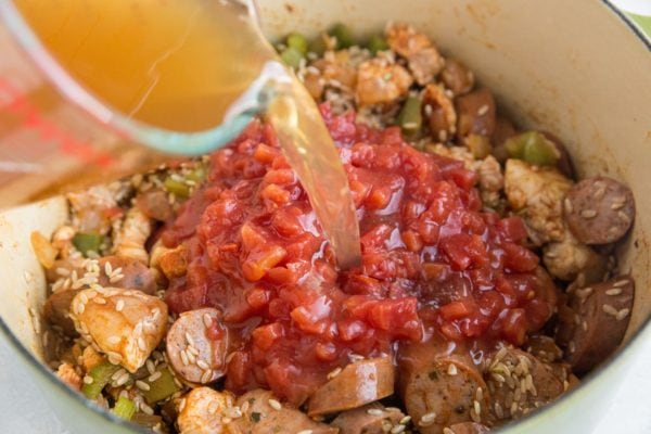 Chicken broth being poured into the pot of Jambalaya ingredients