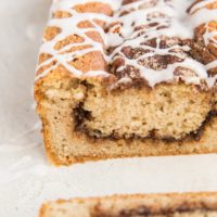 Loaf of low-carb cinnamon swirl bread sitting on a white surface with a slice taken off