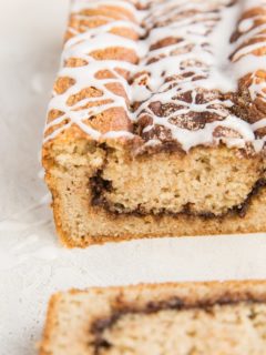 Loaf of low-carb cinnamon swirl bread sitting on a white surface with a slice taken off