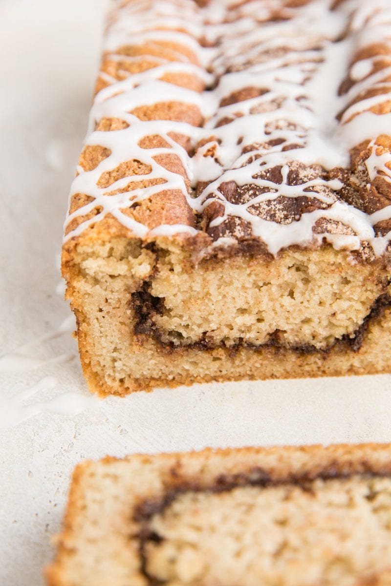 Loaf of low-carb cinnamon swirl bread sitting on a white surface with a slice taken off