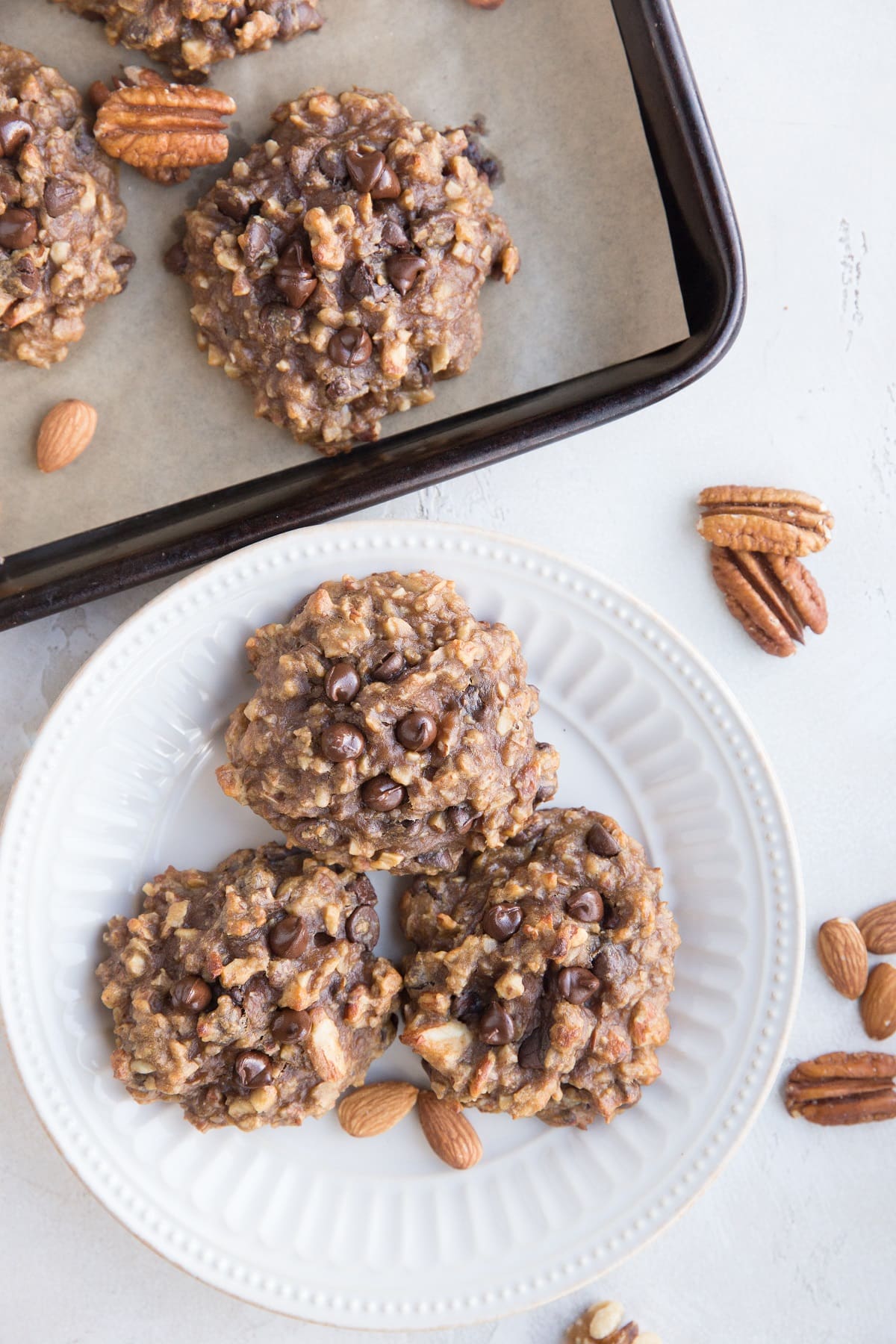 White plate with three banana nut cookies on top with a baking sheet of nutty cookies