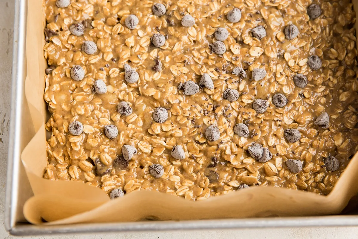 Oatmeal bar mixture in a parchment lined baking pan ready to go into the oven