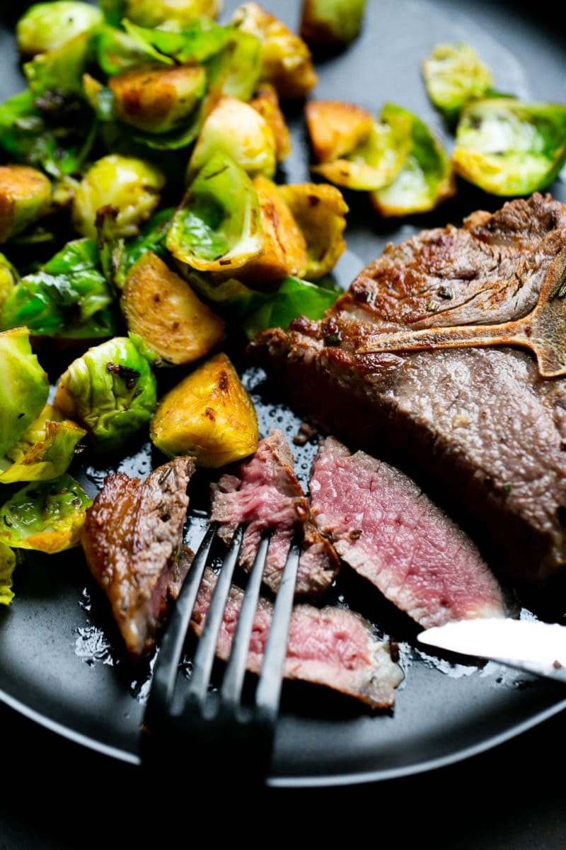 Lamb loin chop being cut with brussels sprouts off to the side