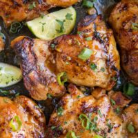 Close up image of Asian Boneless Baked Chicken Thighs with green onion sprinkled on top and some limes