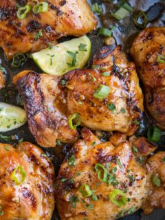 Close up image of Asian Boneless Baked Chicken Thighs with green onion sprinkled on top and some limes