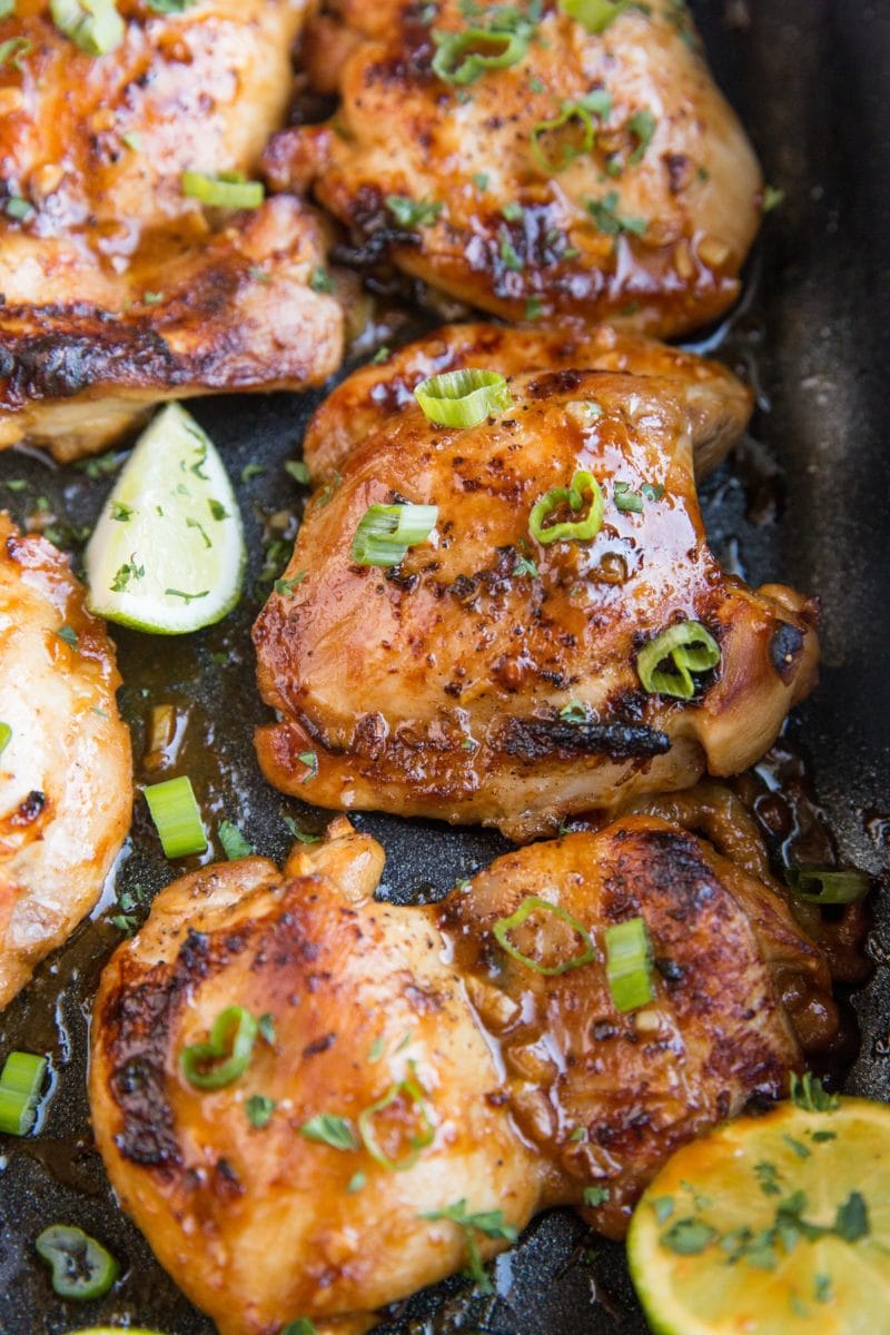 Photo of Asian baked chicken thighs in a casserole dish with green onion slices and slices of lime