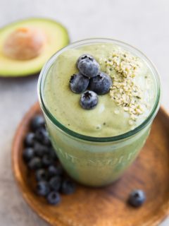 Green avocado smoothie in a glass with blueberries and hemp seeds on top