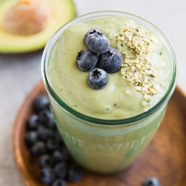 Green avocado smoothie in a glass with blueberries and hemp seeds on top