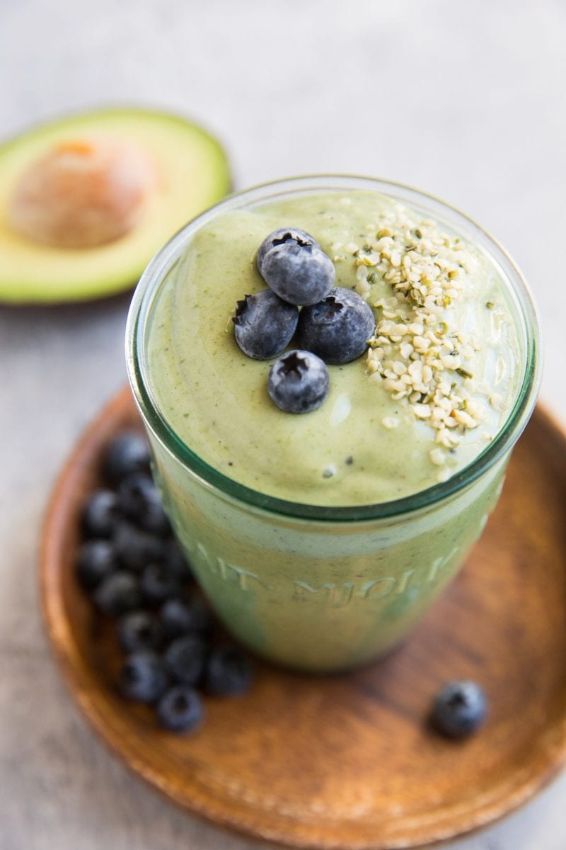 Green avocado smoothie in a glass with blueberries and hemp seeds on top