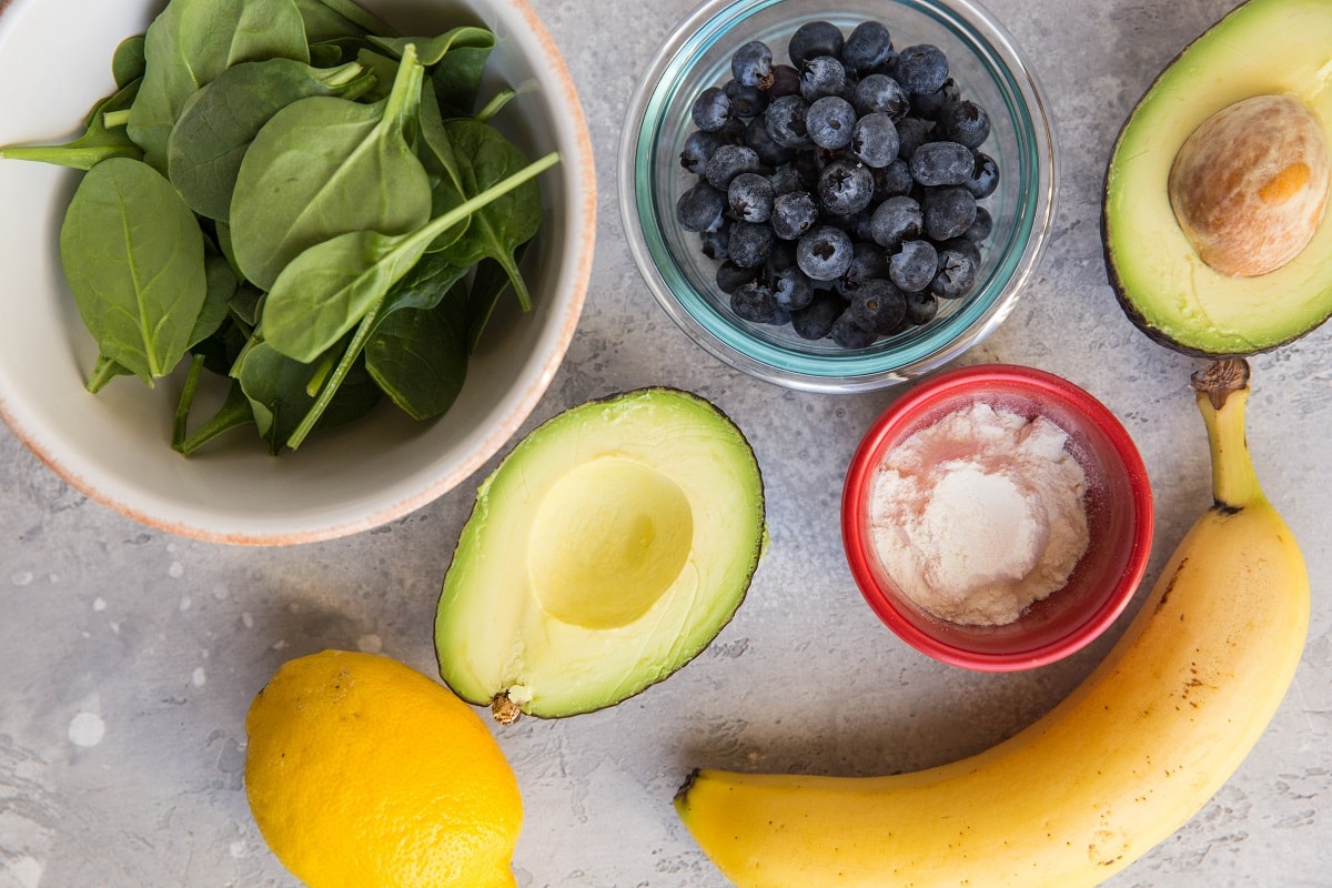 Individual ingredients for avocado smoothie recipe sitting on a backdrop, ready to be blended