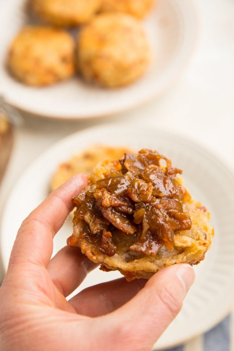 Hand holding a biscuit with bacon jam on top.