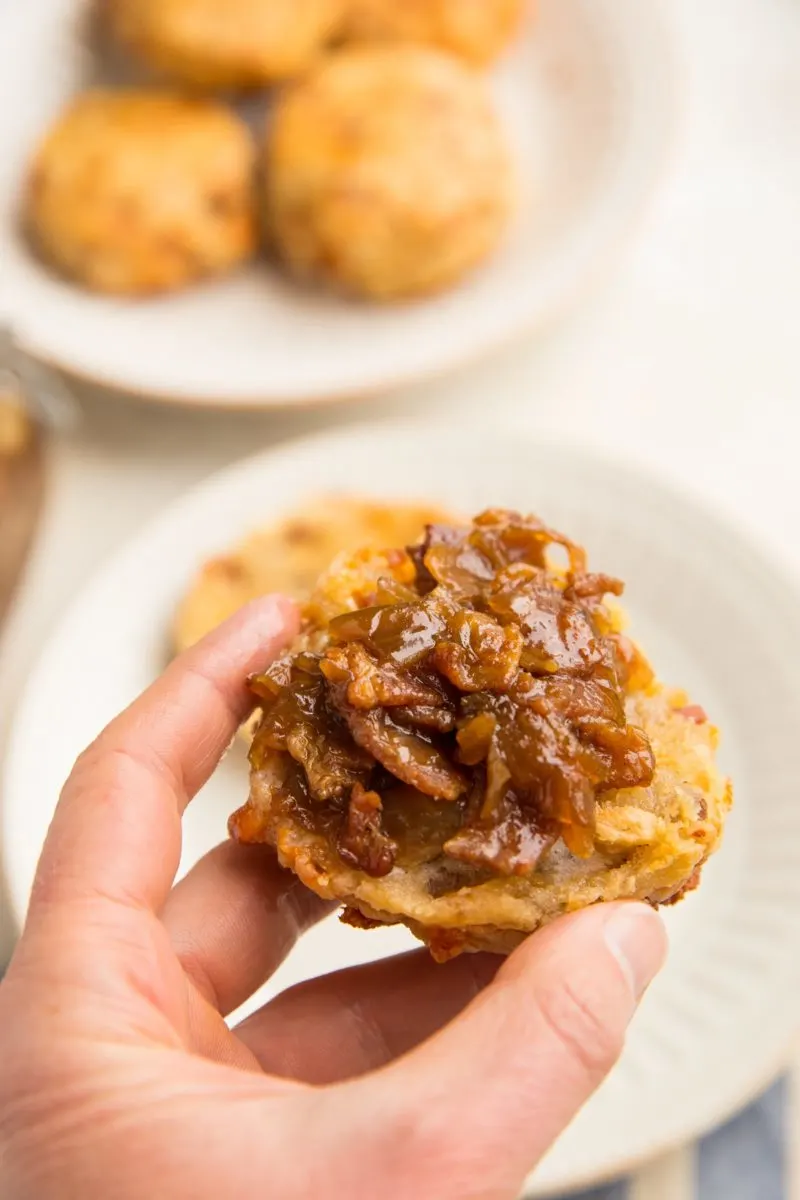 Hand holding a biscuit with bacon jam on top.