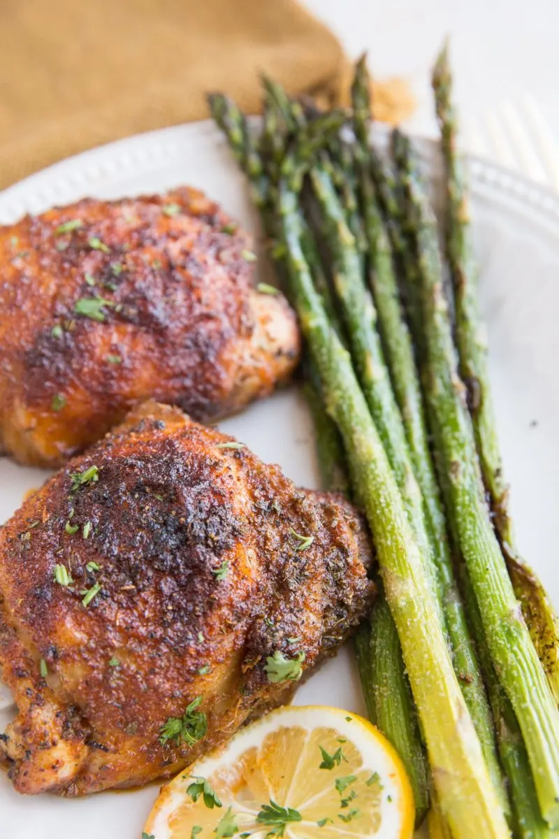 Two blackened chicken thighs on a plate with asparagus