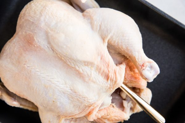 Whole chicken in a roasting pan with a spoon between the skin and the flesh