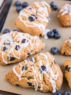 Baking sheet of blueberry almond flour scones with fresh blueberries and a glaze