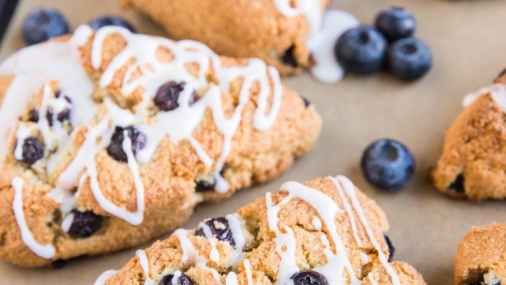 Baking sheet of blueberry almond flour scones with fresh blueberries and a glaze
