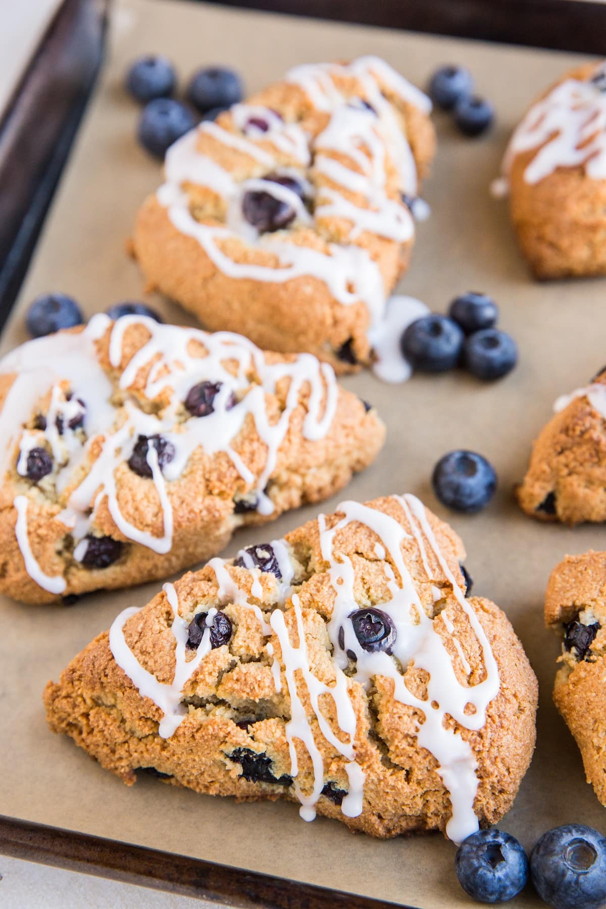 Baking sheet of blueberry almond flour scones with fresh blueberries and a glaze