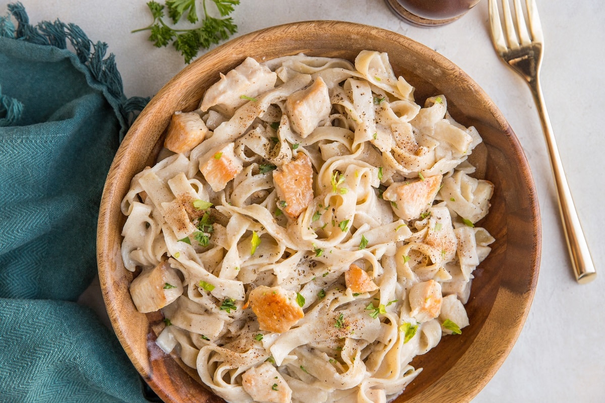 Horizontal image of wooden bowl of alfredo noodles with chicken