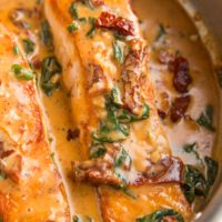 Salmon filets in a skillet with sun-dried tomato sauce.