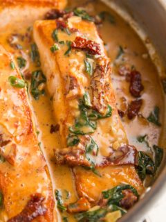 Salmon filets in a skillet with sun-dried tomato sauce.