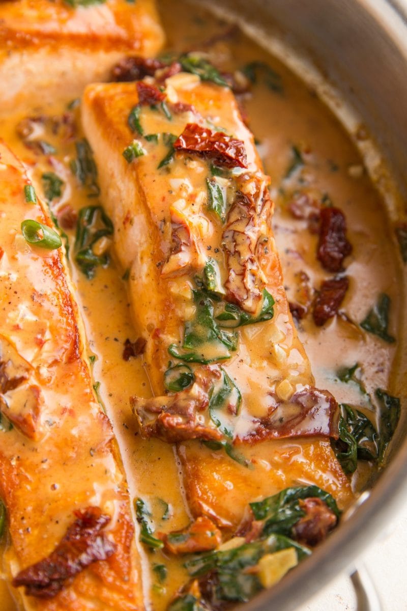 Salmon filets in a skillet with sun-dried tomato sauce.