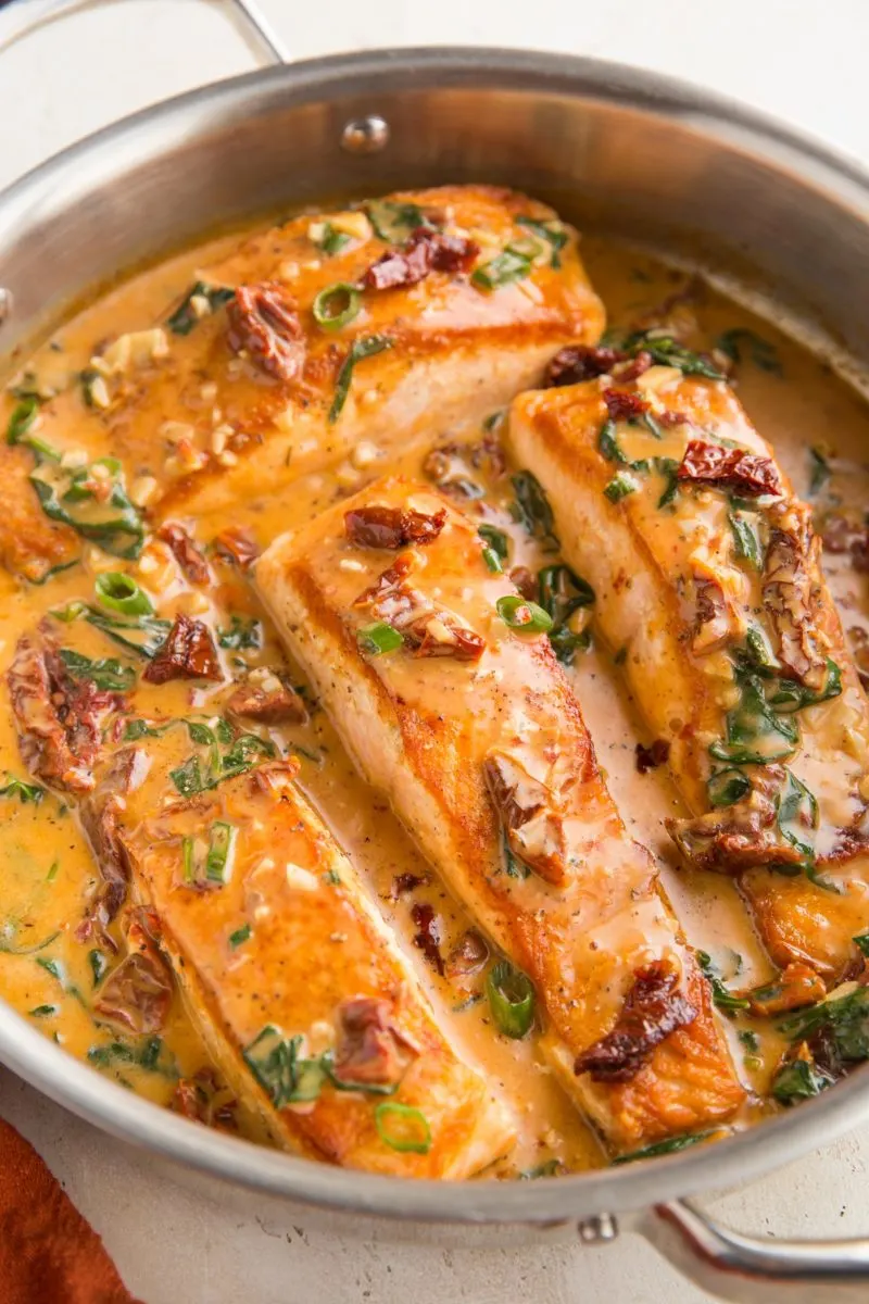 Photo of a stainless steel skillet with four salmon filets in creamy Tuscan sauce