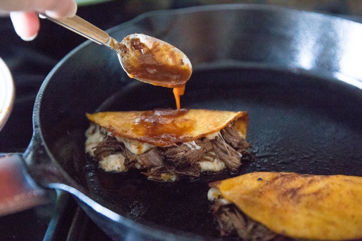 Sauce being poured on a taco as it is pan frying