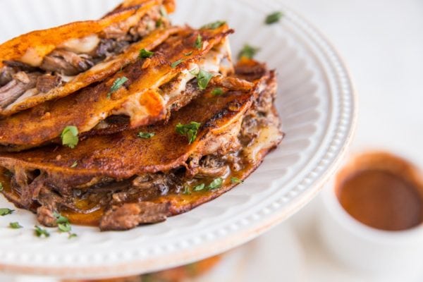 Birria tacos on a plate with dipping sauce to the side