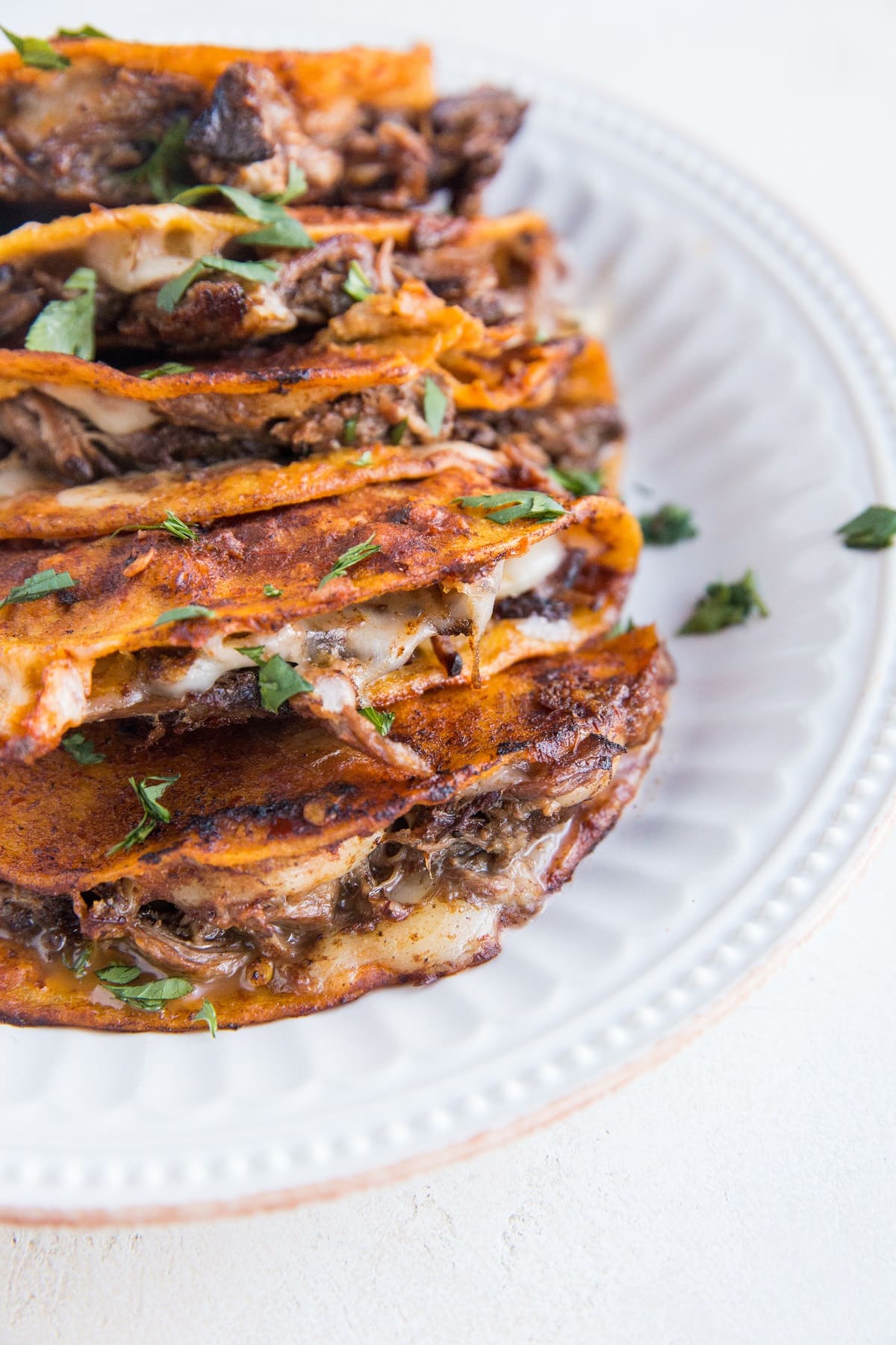 Stack of birria tacos on a white plate with a white background