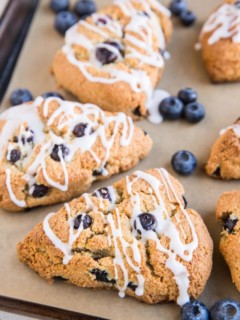 Baking sheet of blueberry almond flour scones with fresh blueberries and a glaze