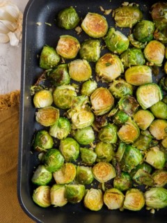 Roasted Brussel Sprouts in a cast iron casserole dish with lemon and garlic off to the side and a brown napkin