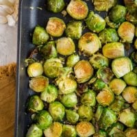 Roasted Brussel Sprouts in a cast iron casserole dish with lemon and garlic off to the side and a brown napkin