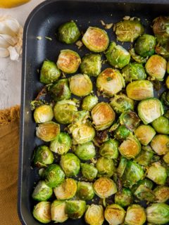 Roasted Brussel Sprouts in a cast iron casserole dish with lemon and garlic off to the side and a brown napkin