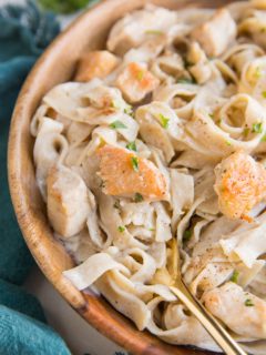 Close up image of creamy chicken fettuccine alfredo in a wooden bowl with a blue napkin and a gold fork