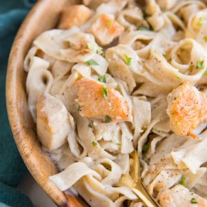 Close up image of creamy chicken fettuccine alfredo in a wooden bowl with a blue napkin and a gold fork