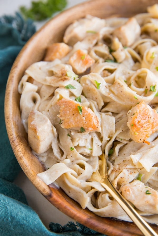 Close up image of creamy chicken fettuccine alfredo in a wooden bowl with a blue napkin and a gold fork